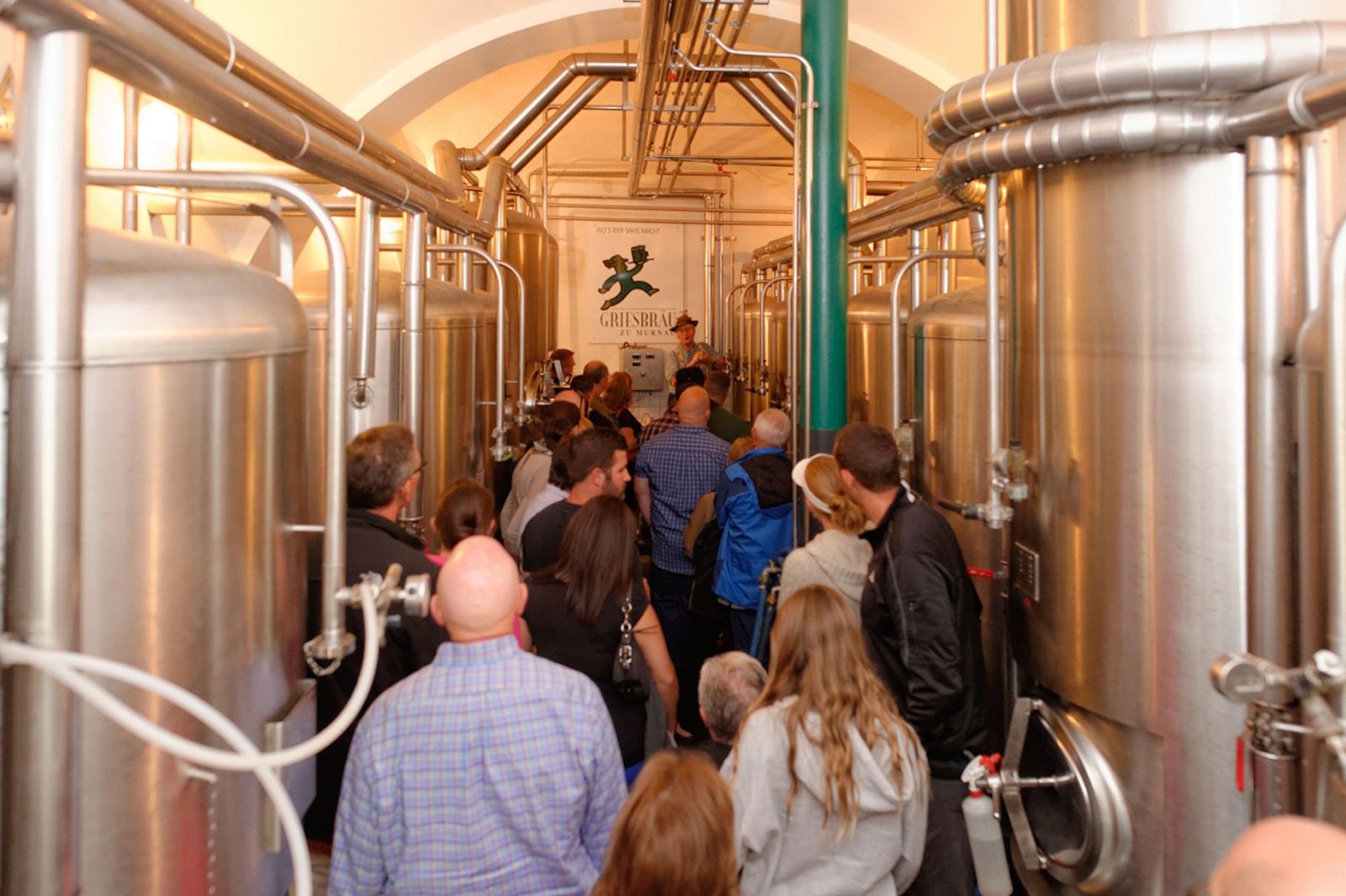 Besuchergruppe bei einer Brauereiführung im Gang zwischen den silbernen Gärtanks der Griesbräu-Hausbrauerei