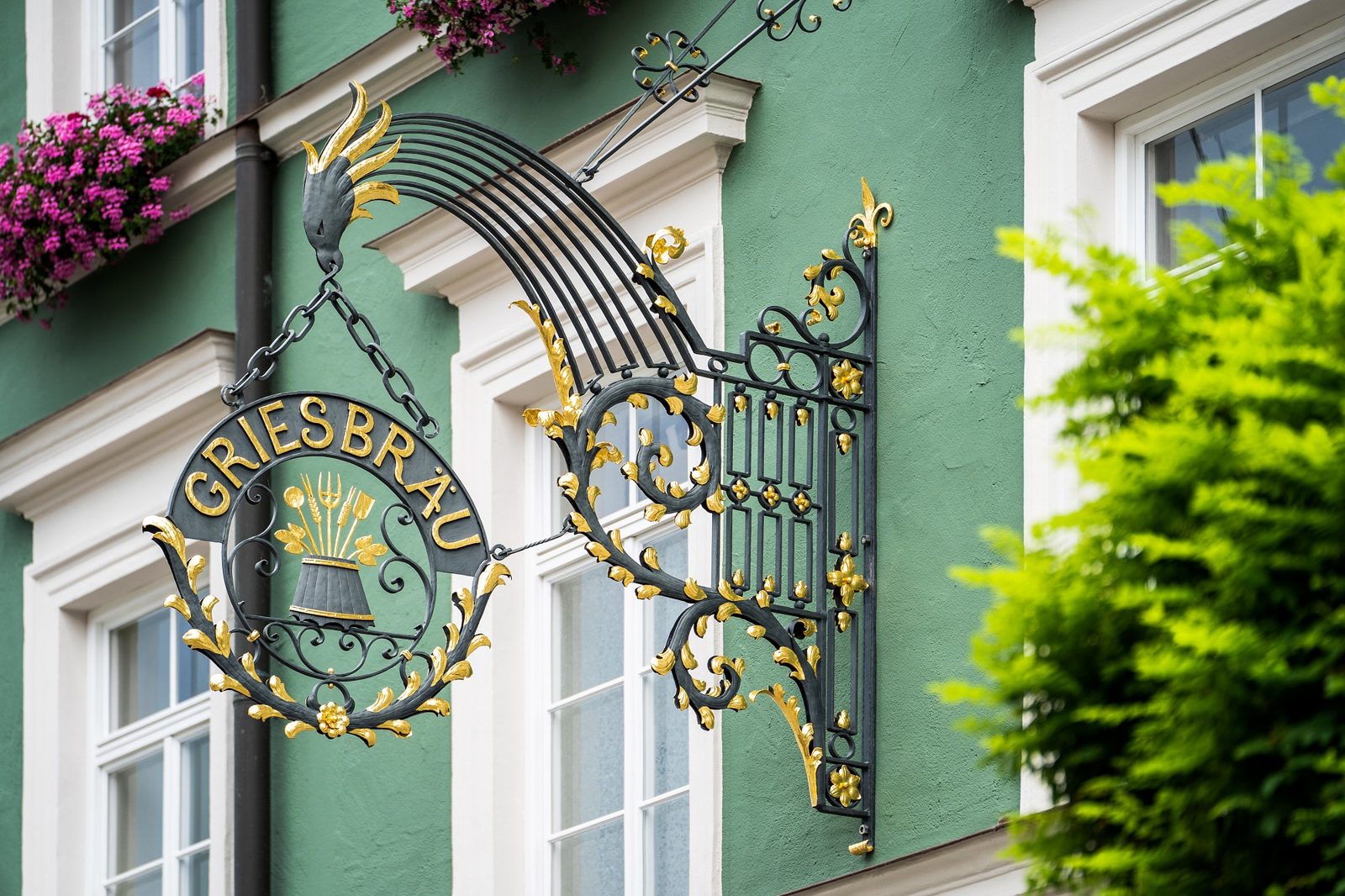 Kunstvoll geschmiedetes Griesbräu-Wirtshausschild an der grünen Fassade des Haupthauses am Obermarkt in Murnau